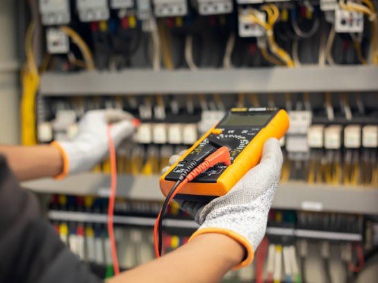 Electrician engineer uses a multimeter to test the electrical installation and power line current in an electrical system control cabinet.
